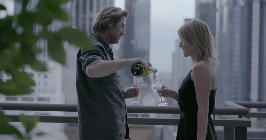 A man and woman celebrate with champagne on a balcony