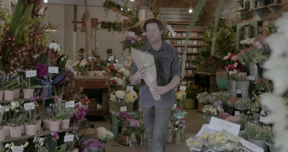 Smiling man walks through a flower shop holding a bouquet