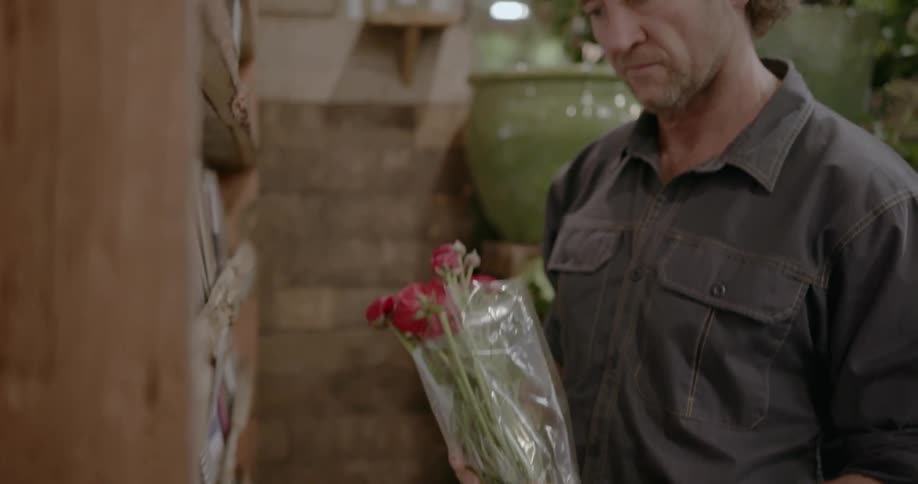A man holding a bouquet looks at cards in a florist shop
