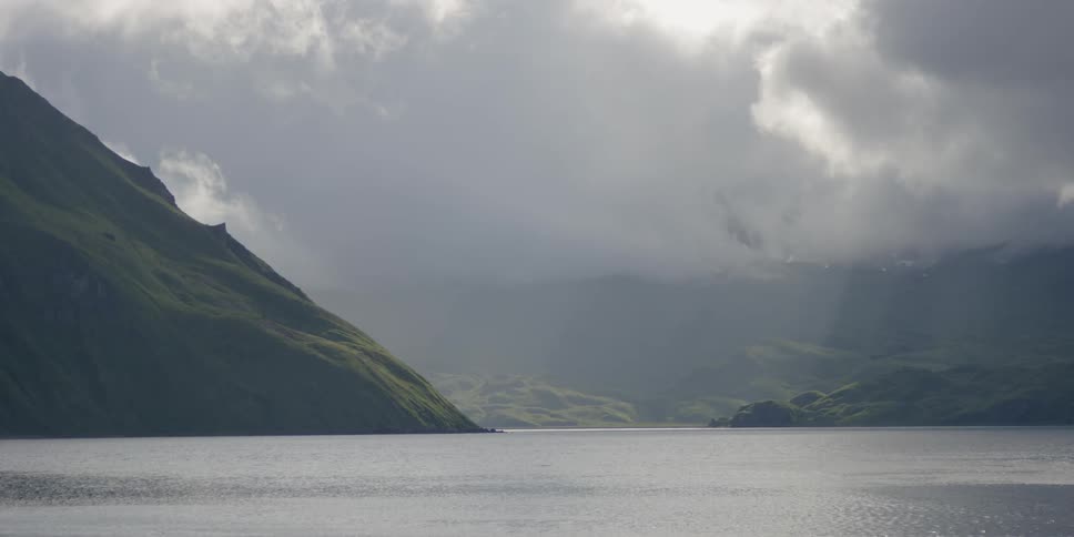 Clouds are hanging above a mountain range and coastline on a stormy day
