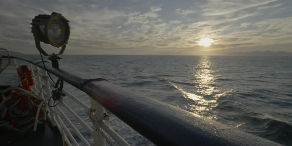 A ship is sailing across the ocean at dawn on a cloudy day