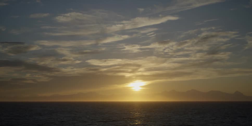 The sun is rising over coastal mountains on a cloudy day