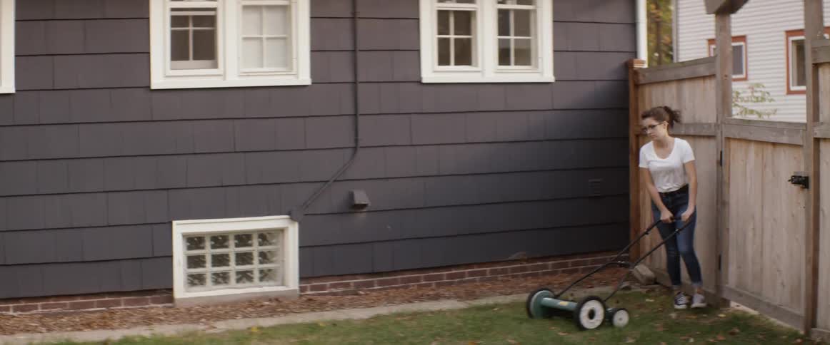 A young woman mows the lawn with a vintage mower