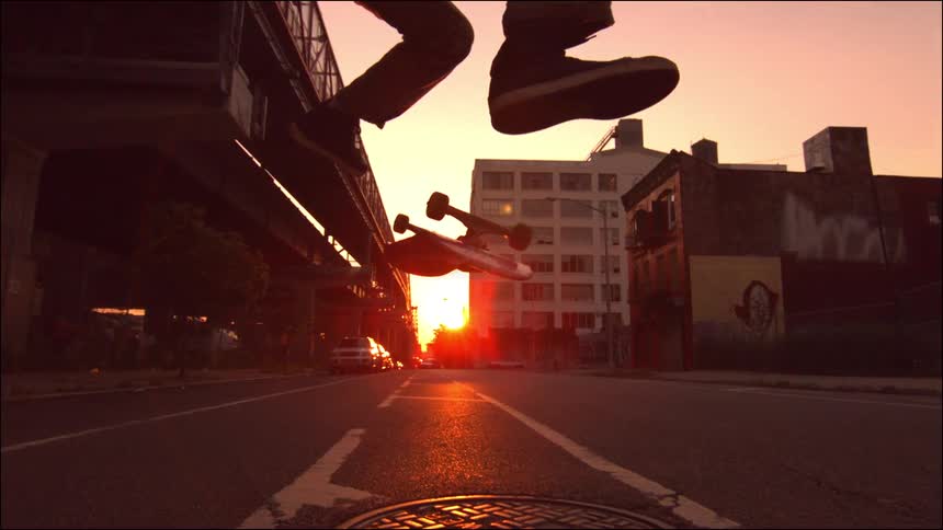 A boy does skateboard tricks on a quiet city street at sunset