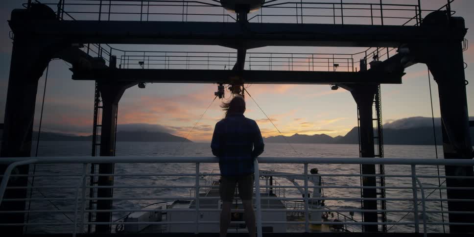 A man stands in the wind on the boat watching the sunset