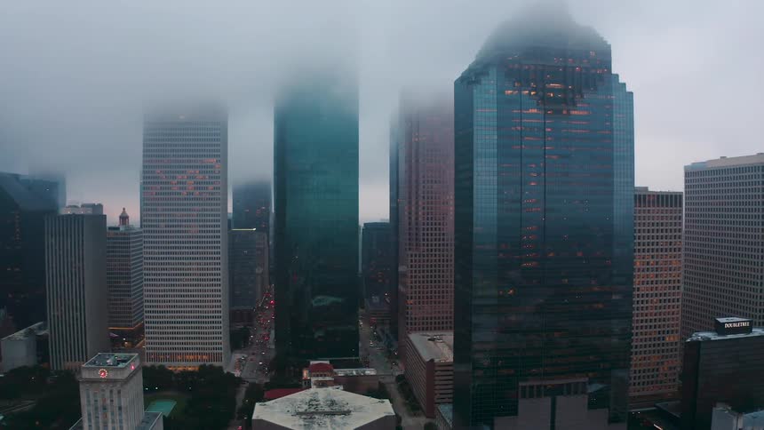 Clouds are hanging above the tops of skyscrapers in a city at dusk
