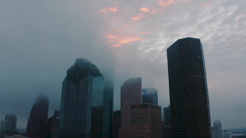 Clouds are hanging above the tops of skyscrapers in a city at dusk