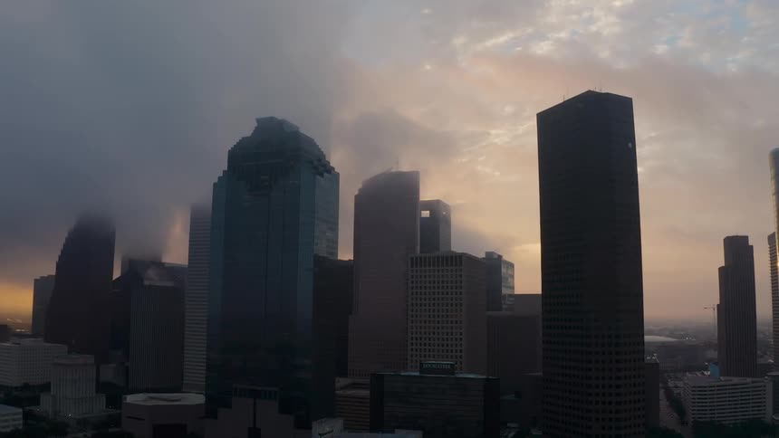 Clouds are drifting over the tops of skyscrapers in a city at dusk