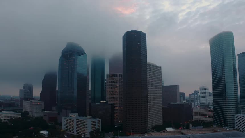 Clouds are drifting over the tops of skyscrapers in a city at dusk