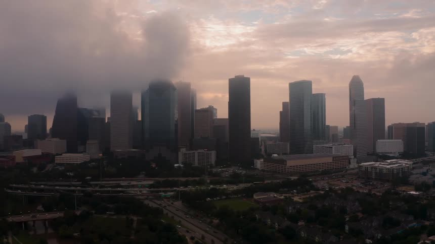 Clouds are hanging above the tops of skyscrapers in a city at dusk