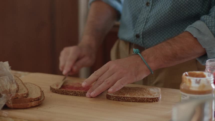 A man is making a peanut butter and jelly sandwich