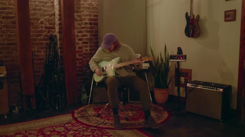 Man sitting down on a stool to play his guitar indoors