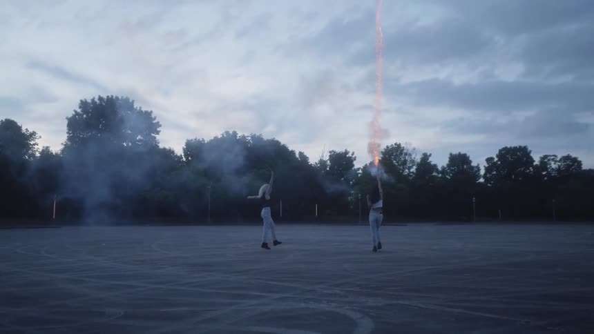 Two women in a field shooting a flare into the air on a cloudy day