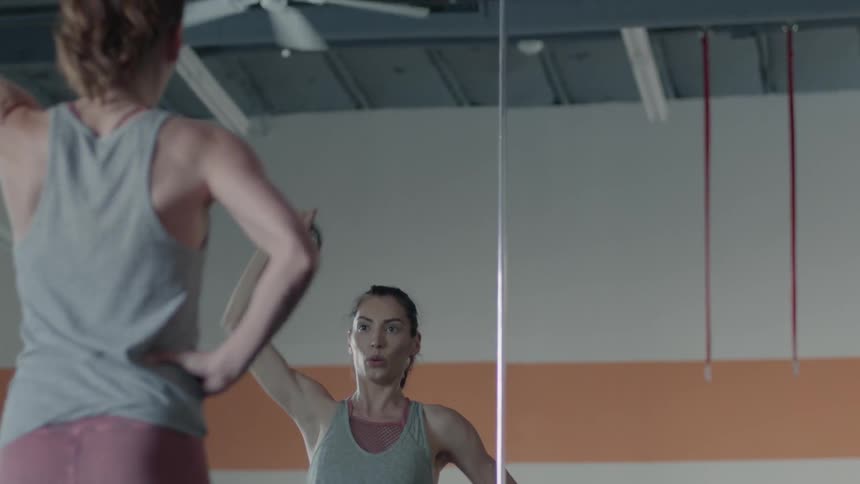 A woman is lifting a kettlebell weight above her head as she stands in a gym during the day