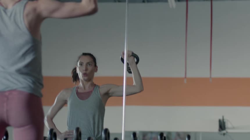A woman works out in a gym in front of mirrors