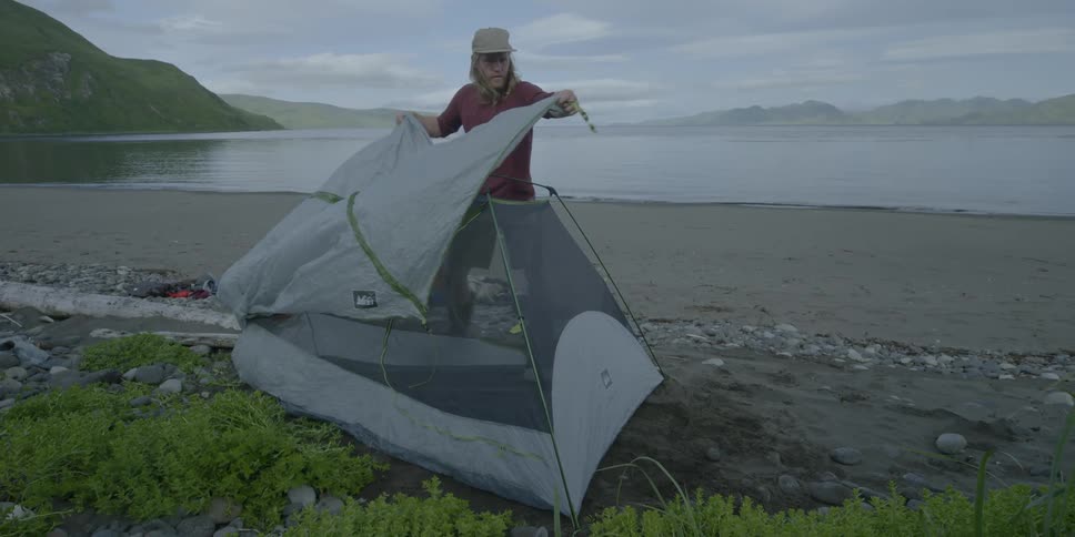 A camper puts a rain fly over a tent