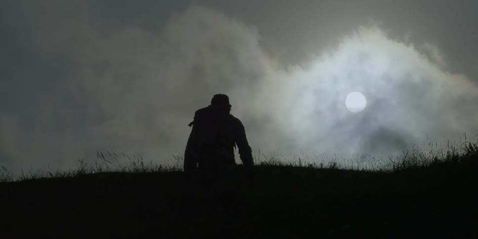 Silhouetted hiker climbs up a grassy hill