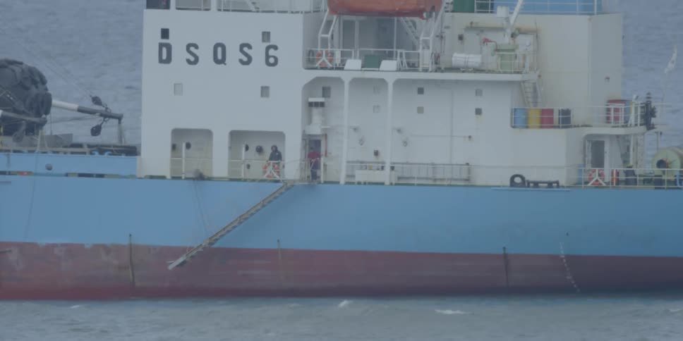 People stand on the deck of a ship moving through the ocean