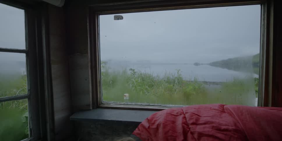 A man rests in a sleeping bag in an ocean shack