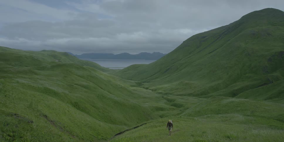 A man hikes through rolling green fields