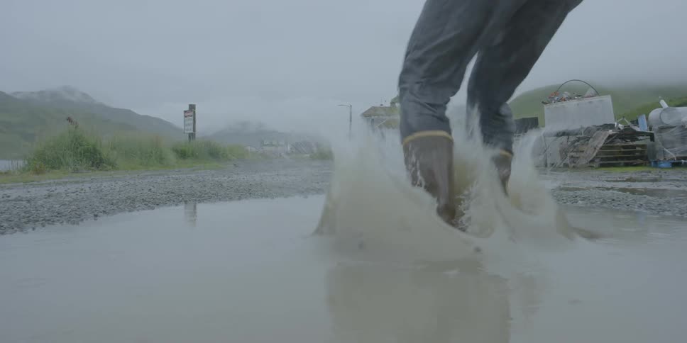 Person jumping and splashing into a big puddle before running on a cloudy day