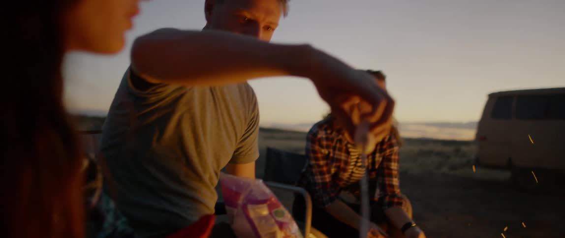 A group of people talk and roast marshmallows around a campfire