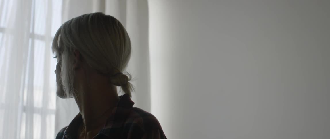 A blond haired woman stands next to a bedroom window