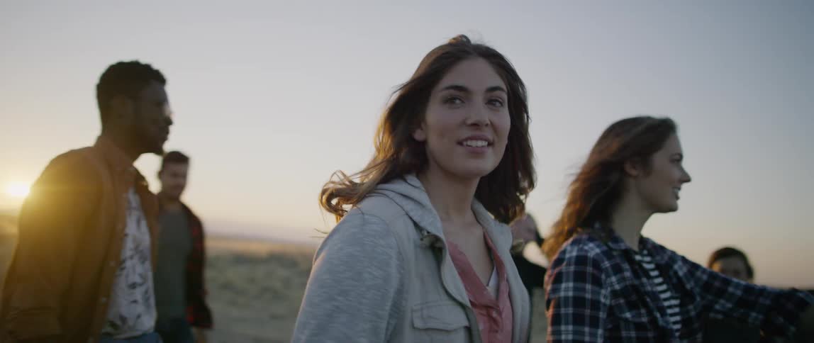 A group of people walk on the grass field at sunset