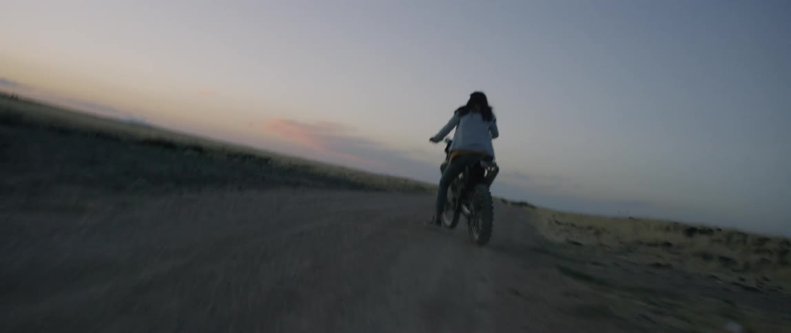 Person rides a motorbike down a dirt road at sunset