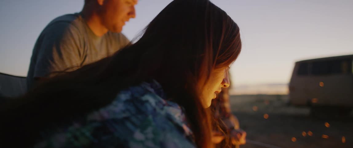 Men and women sit around a campfire on the beach at sunset