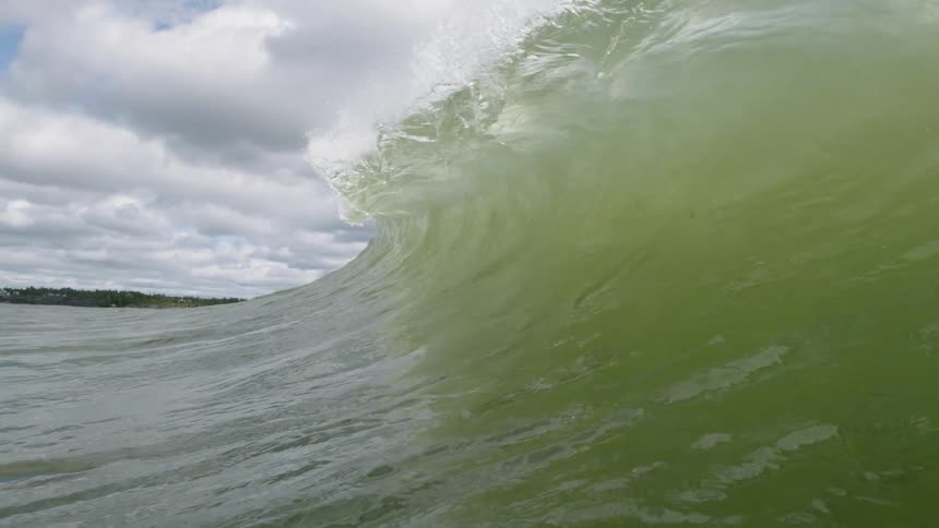 A large waves crashes forward on a cloudy day
