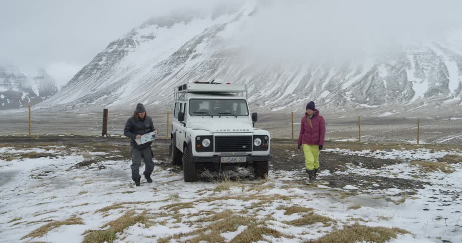 People exit a white truck by the snowy mountains