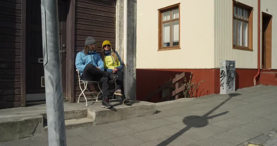 A couple are sitting outside a building talking on a cold sunny day