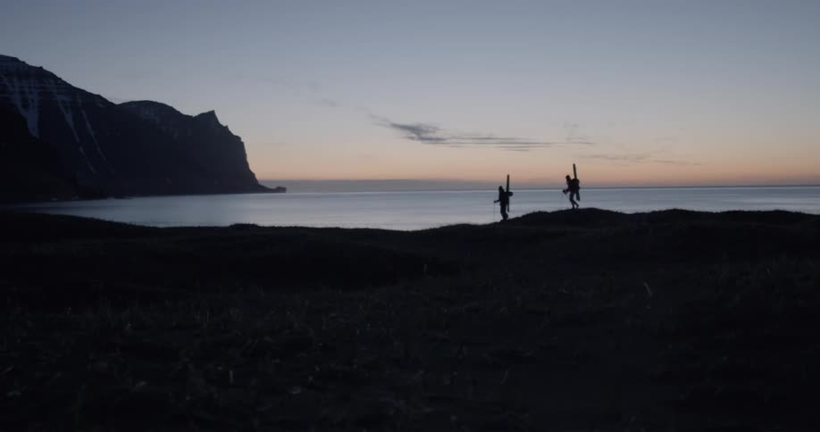People with backpacks are walking next to the ocean at dusk