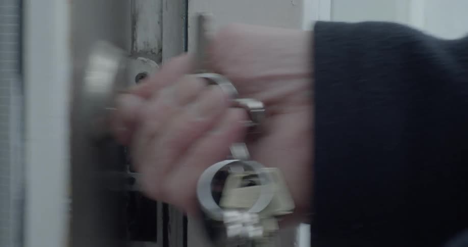A person unlocks a door with keys and opens it