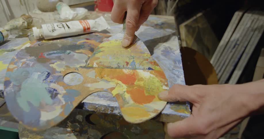 A painter is cleaning a palette with a scraper
