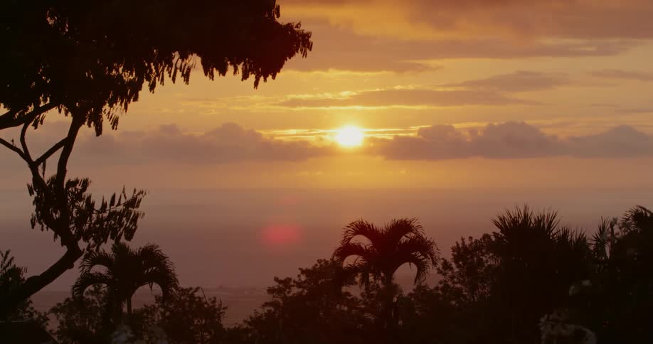 The warm sun begins to set behind clouds over the ocean