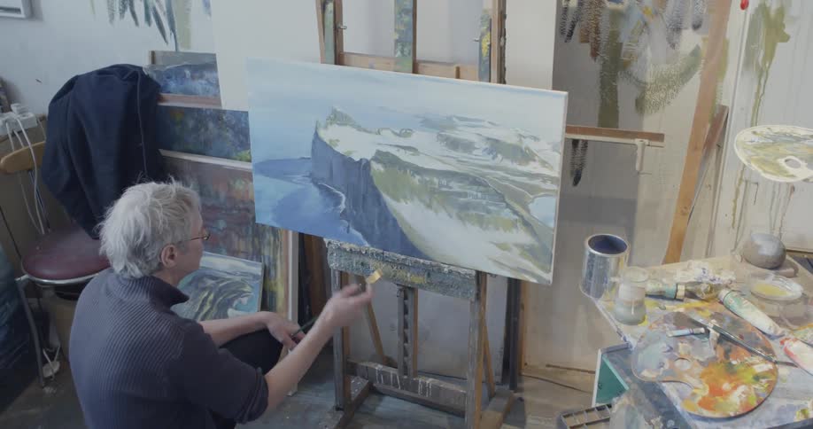 Man paints a mountain scene in an art studio