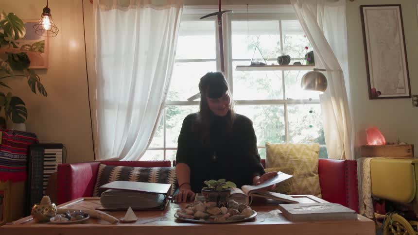 A woman is sitting at a living room table leafing through a book during the day