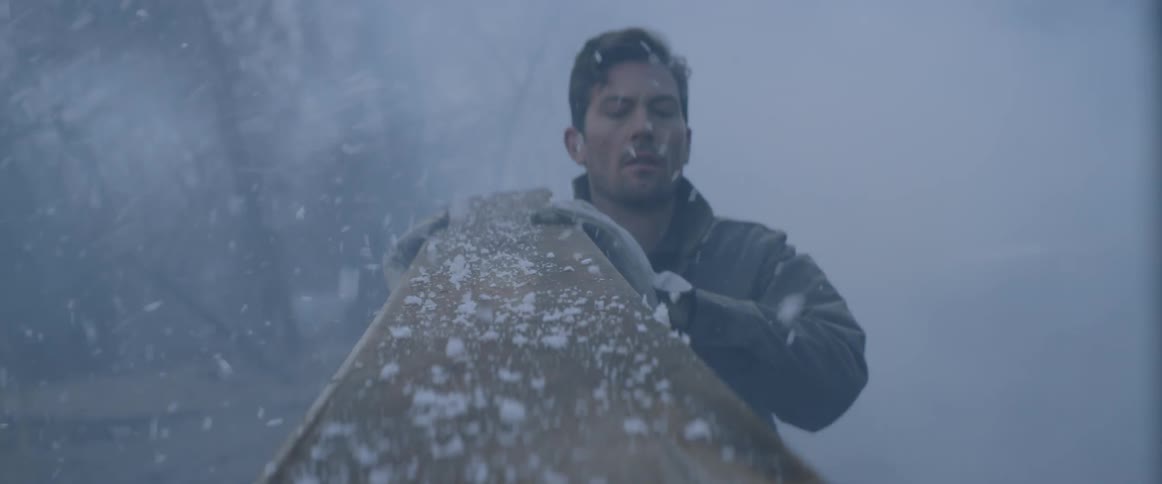 A man is moving a piece of wood outside as it snows
