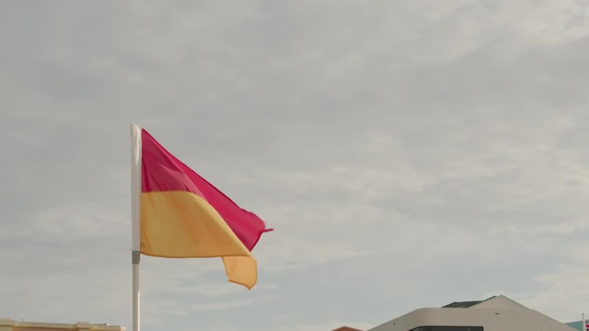 A red and yellow flag waves slowly in the wind