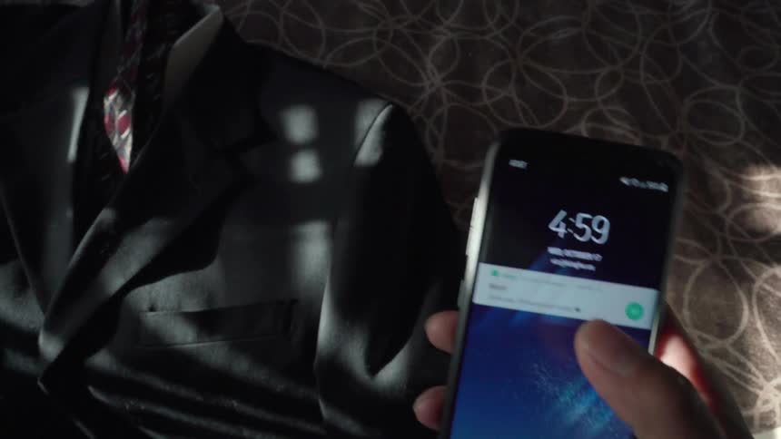 Man places a suit on a bed and picks up a smartphone