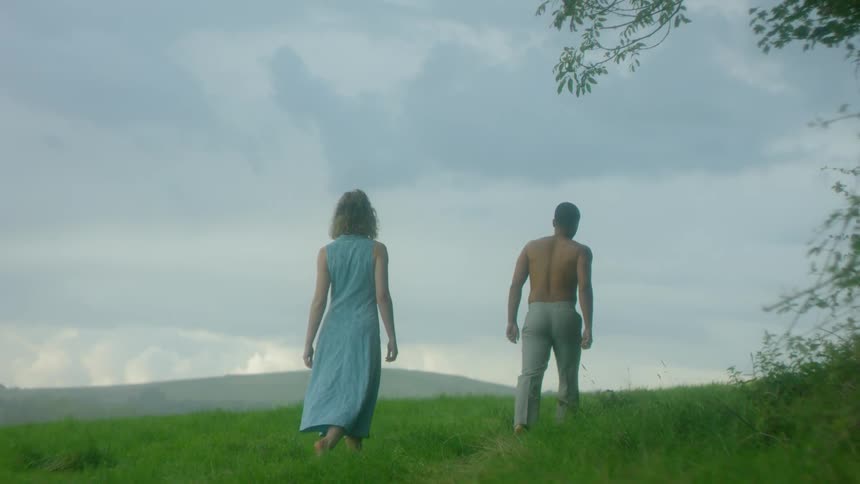 A man and woman are walking on a hillside under cloudy skies at dusk