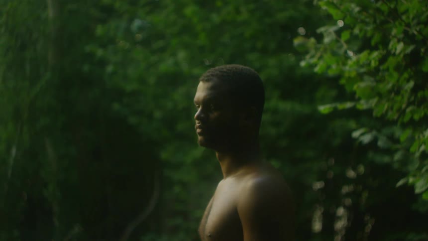 A shirtless man standing in the woods turns around