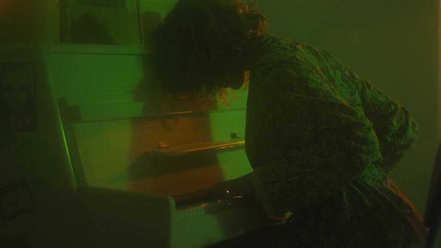 A woman who is sitting is leaning over a piano in the dark