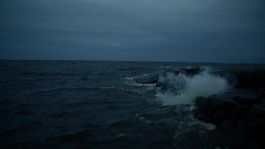 Waves crash against rocks at dusk on a cloudy evening
