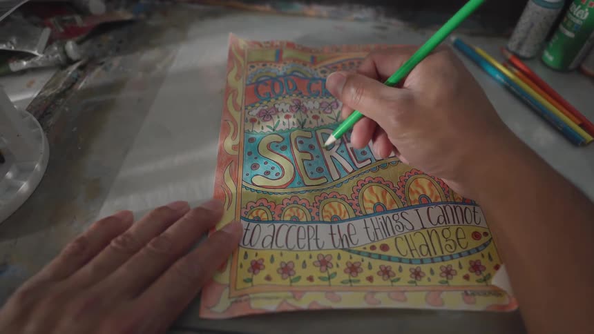 An artist draws on paper with colored pencils