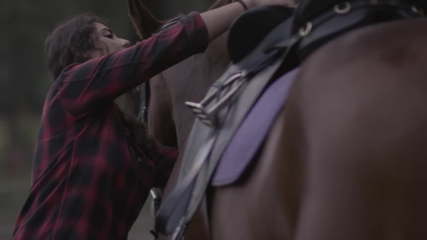 A woman secures a saddle on a horse