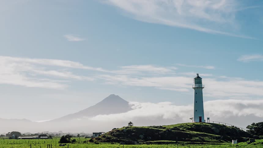 Clouds rolling over a mountain near a lighthouse