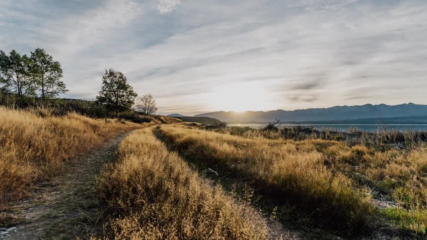 Clouds are drifting over a dirt trail near mountains at dawn